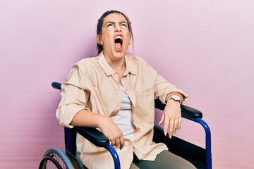 Canvas Print - Young hispanic woman sitting on wheelchair angry and mad screaming frustrated and furious, shouting with anger. rage and aggressive concept.