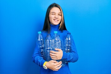 Poster - Young brunette girl holding recycling plastic bottles winking looking at the camera with sexy expression, cheerful and happy face.