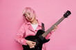 © wayhome.studio  - Cool stylish female rocker plays famous song on electric guitar tilts head has pink hair floating on wind demonstrates her talent wears jacket isolated over rosy studio background. Musical instruments