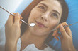 © rogerphoto - Smiling brunette woman being examined by dentist at dental clinic. Hands of a doctor holding dental instruments near patient's mouth. Healthy teeth and medicine concept