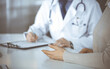 © rogerphoto - Unknown male doctor and patient woman discussing something while sitting in clinic and using clipboard. Best medical service in hospital, medicine, pandemic stop