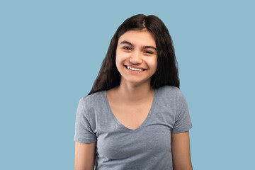 beautiful indian teenage girl with dark long hair smiling and looking at camera on blue studio backg