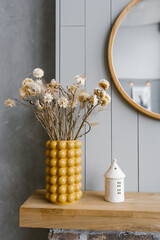 Dried flowers in a yellow ceramic vase in the interior decor of a Scandinavian house with gray walls.