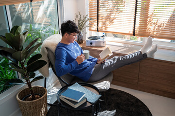 Handsome Asian Man wearing eyeglasses and smiling while Reading Book At Home living room lounge, literature and leisure concept