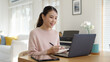 © ChayTee - Candid young attractive beautiful asian businesswoman work remotely from home or learning online sitting smiling in cozy workspace at home feeling happy in quarantine social distance concept.