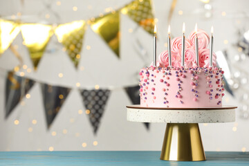 Beautifully decorated birthday cake on turquoise wooden table against blurred festive lights, space for text