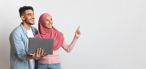 Online Offer. Cheerful Muslim Couple With Laptop Pointing Aside At Copy Space