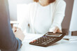 © Iryna - Accountant checking financial statement or counting by calculator income for tax form, hands closeup. Business woman sitting and working with colleague at the desk in office. Tax and Audit concept