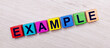 On a light wooden background on multi-colored bright wooden cubes the word EXAMPLE