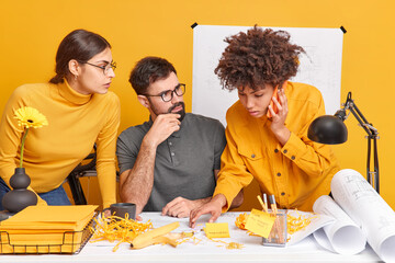 Team od mixed race two women and one man try to create new strategies try to solve problems while doing sketches of future building. Afro American woman calls partnes via smartphone asks for advice