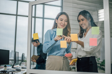 Asian two woman smiling and using post it notes to share about project.