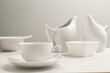 Cup of tea on a white table. A set of white dishes, milk jug and white jug against a grey background.