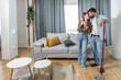 © Srdjan - Young happy satisfied couple standing in their apartment with cleaning broom or mop hugging after finishing with cleansing of dust and dirt from their floor