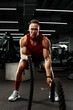 © Georgii - Sport. Strong man exercising with battle ropes at the gym with. Athlete doing battle rope workout at gym. Dramatic sports background.