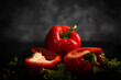 Rote Paprika liegt auf den Salatblättern, auf dem schwarzen Hintergrund. Eine Paprika ist durchgeschnitten, die zweite ist im Stück.Querformat