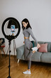 © shevtsovy - Attractive Woman virtual fitness workout at home. fitness influencer. Fitness workout exercises online women at home. Fitness influencer personal trainer coach recording on smartphone camera new