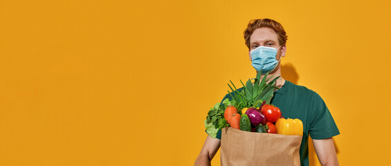 Young caucasian courier in mask holding fresh vegetables