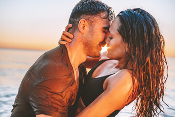 Happy young fit couple embrace each other with love in the sea or ocean at summer sunset. Romantic mood, tenderness, relationship, vacation concept.