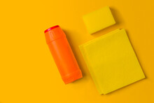 Yellow And Orange Cleaning Sponges And Bottles Of Detergent On A Yellow Background With Copy Space. Household Chores Or House Cleaning Services. Cleaning Products Concept