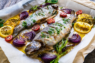 Sheet pan dinner - roasted whole trouts with lemon ,rosemary, tomatoes, red onion and potatoes on cooking pan on wooden table
