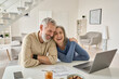 © insta_photos - Happy mature older family couple laughing, bonding sitting at home table with laptop. Smiling middle aged senior 50s husband and wife having fun satisfied with buying insurance, paying bills online.