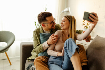 Wall Mural - Caucasian couple is taking a selfie while they are smiling and looking to each other.