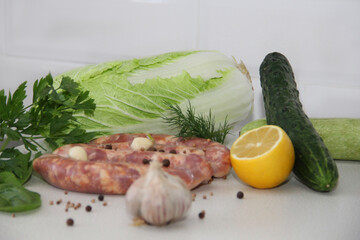 raw meat natural sausages with seasonings,spices and herbs, cabbage,cucumber,lemon, zucchini, garlic and parsley on a bright table