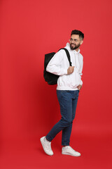 Wall Mural - Young man with stylish backpack walking on red background