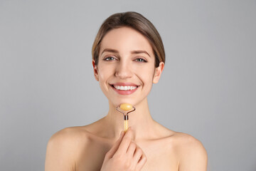 Canvas Print - Young woman using natural jade face roller on light grey background