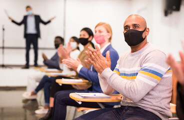 Wall Mural - Portrait of male participant of business event in face mask applauding speaker at conference