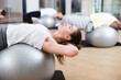 Portrait of positive girl performing set of exercises with pilates ball during group class in fitness studio