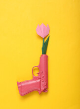 Origami Flower From The Barrel Of A Pink Gun On Yellow Background. Creative Romantic Concept. Minimalism Love Flat Lay. Minimal Layout.Top View