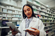 © StratfordProductions - Female african american pharmacist working in chemist checking medicine details in digital tablet