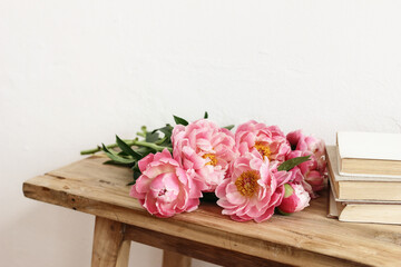 Close-up of pink peonies flowers, bouquet and books. lying on old wooden table. White wall. Selective focus, blurred background. Wedding or birthday celeberation concept. Floral still life scene.