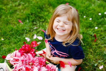 Wall Mural - Cute adorable little toddler girl with lot of pink peony flowers in bucket. Happy smiling child in domestic garden on warm spring or summer day.