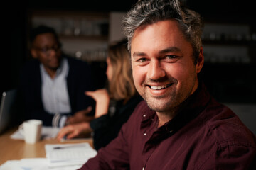 Close-up of smiling mature businessman looking at camera with colleagues at background