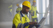 © nimito - Portrait of handsome afro-american builder in helmet sitting with laptop at construction site