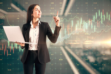 Sticker - Businesswoman holding a laptop in an office corridor, colorful trading raising chart in the background. Stock market and trading concept