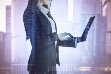 Canvas Print - Businesswoman with a laptop standing thinking with skyscrapers in the background, decision and entrepreneurship concept. Double exposure