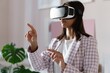 © opolja - Confident young woman in virtual reality headset pointing in the air while standing at her working place in office