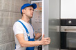 © yaroslav1986 - Uniformed repairman repairs the refrigerator door in the kitchen