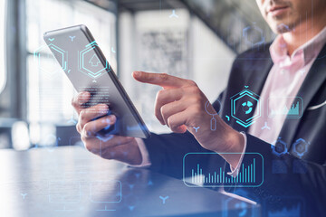 Businessman in suit using tablet device to optimize development by implying new technologies in business process. Interconnections and hi tech hologram over modern panoramic office background