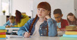 © TommyStockProject - Cute redhead preteen girl in classroom writing in notebook