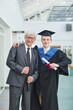 Vertical portrait of smiling young man posing with father during graduation ceremony indoors