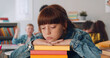 © TommyStockProject - Bored schoolgirl in casualwear keeping her chin on top of stack of books sitting at desk