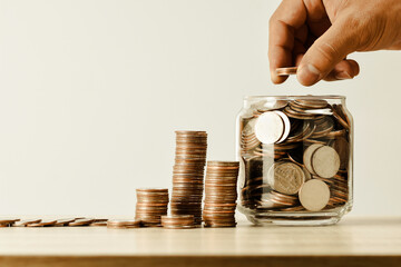 Thai coins are lined up and hand holding money in a jar on the table shown in the form of a graph vintage tone , business and financial, saving concept