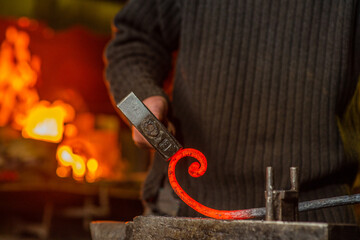 Close-up of the hands of a blacksmith twisting a spiral with a hammer, putting a red-hot iron blank on an anvil. Work in the forge