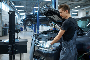 Wall Mural - Male mechanic adjusts the headlights, car service