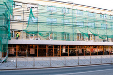 Renovation Of Building Walls, House In Scaffolding And Protective Green Mesh For Safety