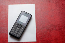 Top View Of An Old-fashioned Black Phone On White Paper On A Red Background.